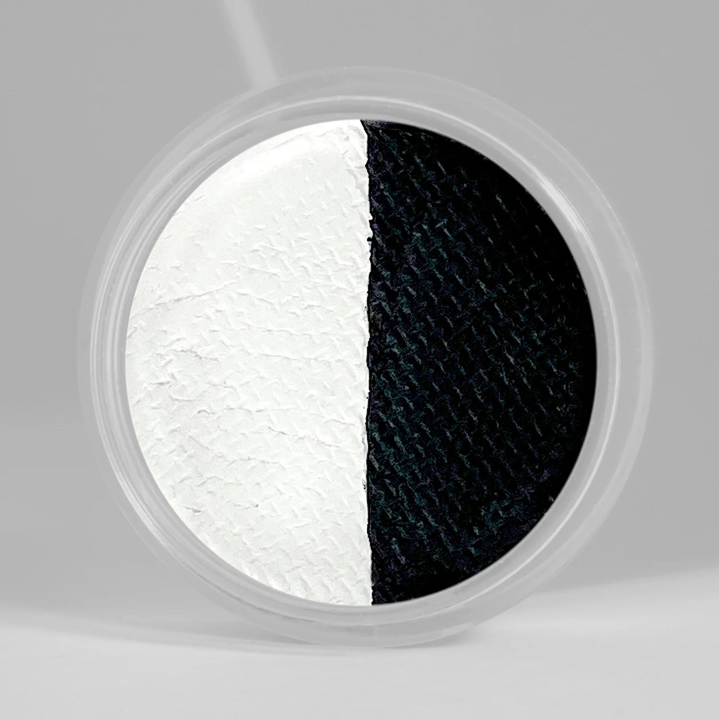 Close up of SUVA's Hydra Liner/FX water activated, cake eye liner pan in shade "Doodle". Split down the center the left half is bright white & the right side is matte black.
