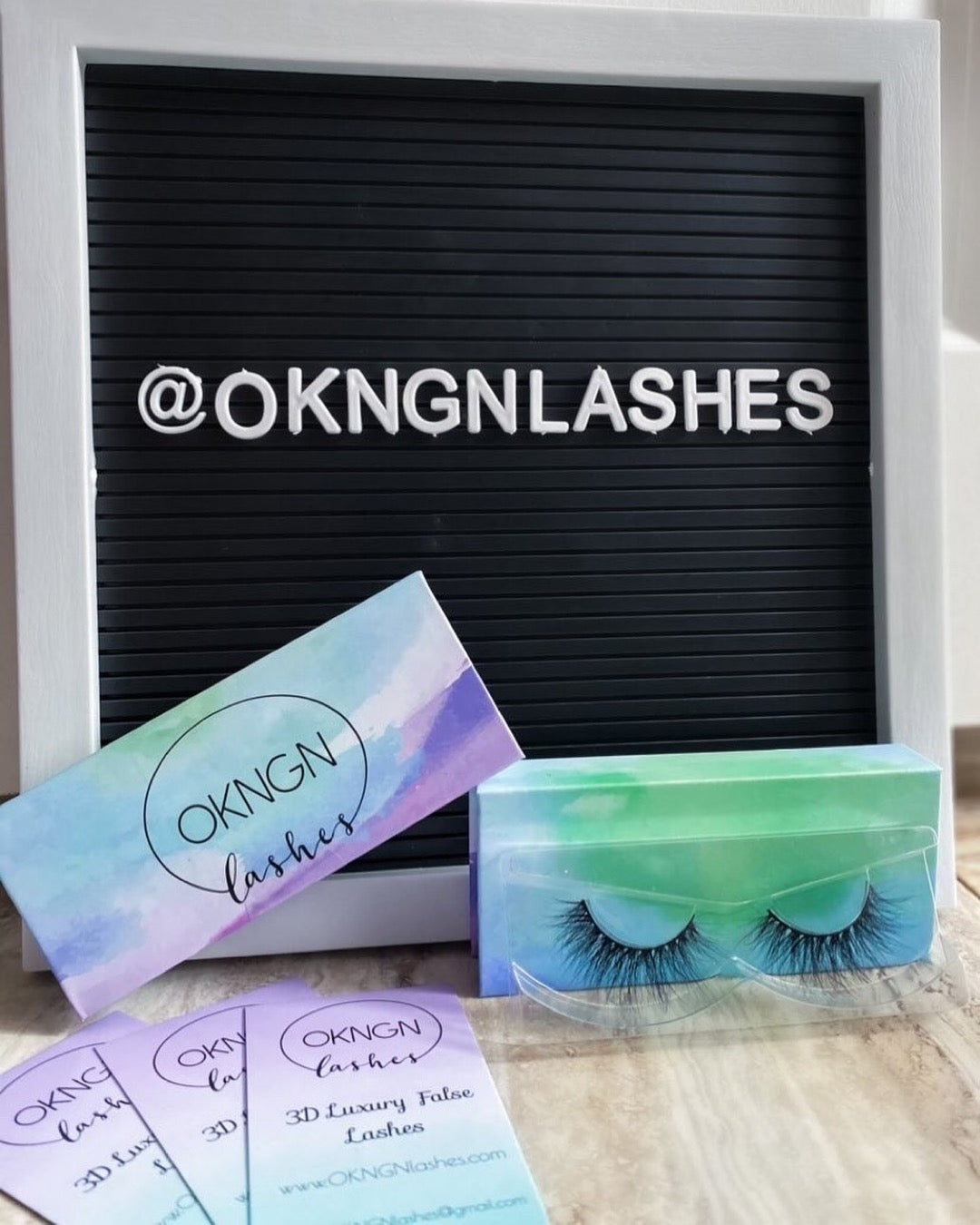 A letter board spelling out @OKNGNlashes with water colour lash boxes and matching business cards in front. 